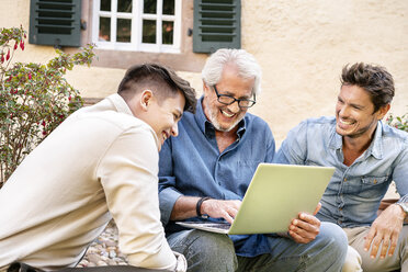 Drei glückliche Männer unterschiedlichen Alters benutzen einen Laptop im Garten - PESF01296