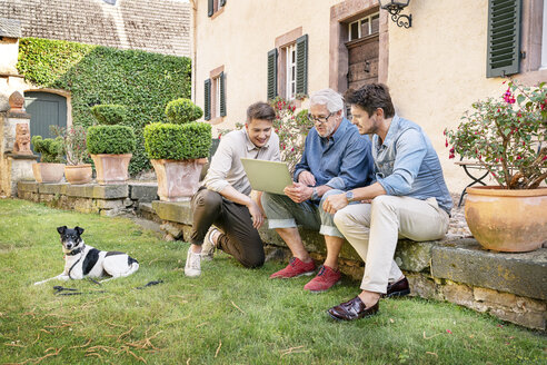 Drei Männer unterschiedlichen Alters sitzen im Garten und benutzen ein Tablet - PESF01297