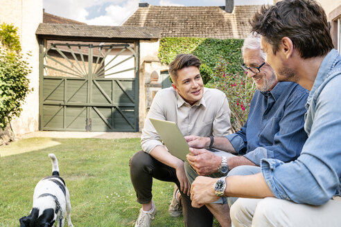 Drei lächelnde Männer unterschiedlichen Alters benutzen ein Tablet im Garten - PESF01298