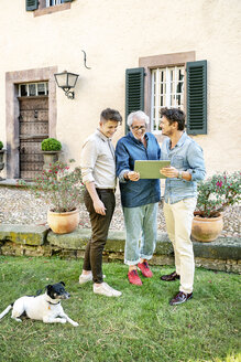 Drei glückliche Männer unterschiedlichen Alters benutzen ein Tablet im Garten - PESF01300