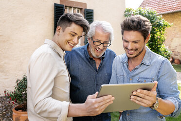 Drei glückliche Männer unterschiedlichen Alters benutzen ein Tablet im Garten - PESF01303