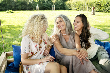 Three happy women of different age sittingon a hanging bed in garden talking - PESF01307
