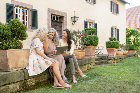 Drei glückliche Frauen unterschiedlichen Alters sitzen im Garten und benutzen ein Tablet - PESF01311