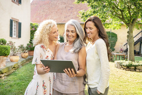 Drei glückliche Frauen unterschiedlichen Alters benutzen ein Tablet im Garten - PESF01312