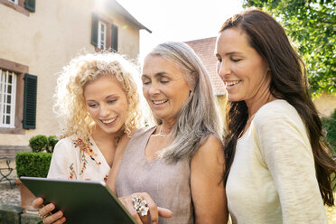 Drei lächelnde Frauen unterschiedlichen Alters benutzen ein Tablet im Garten - PESF01313