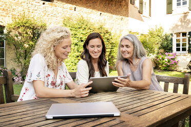 Drei Frauen unterschiedlichen Alters sitzen am Gartentisch und benutzen ein Tablet - PESF01314