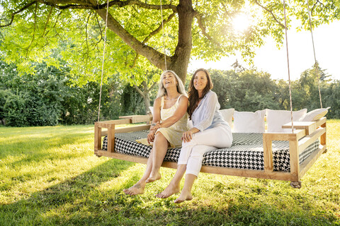 Zwei Frauen entspannen sich auf einem Hängebett im Garten, lizenzfreies Stockfoto