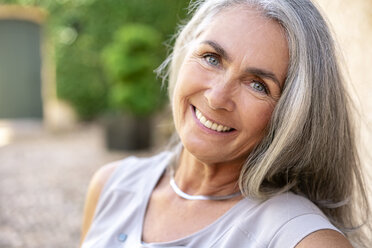 Porträt einer lächelnden Frau mit langen grauen Haaren im Garten - PESF01357