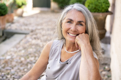 Porträt einer lächelnden Frau mit langen grauen Haaren im Garten - PESF01358