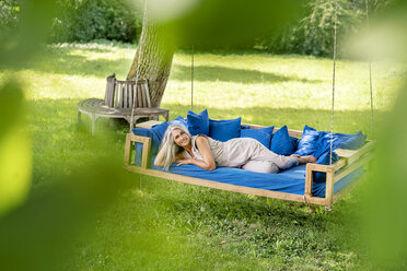 Lächelnde Frau mit langen grauen Haaren liegt auf einem Bett im Garten - PESF01366