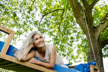 Lächelnde Frau mit langen grauen Haaren liegt auf einem Bett im Garten - PESF01367