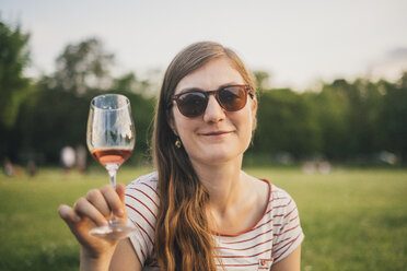Portrait of smiling woman wearing sunglasses toasting with glass of wine at city park - JSCF00134