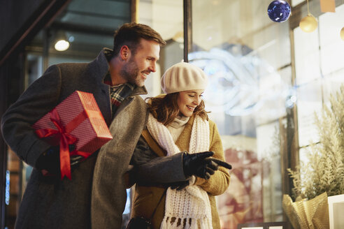 Smiling couple looking in shop window at Christmas time - ABIF01153