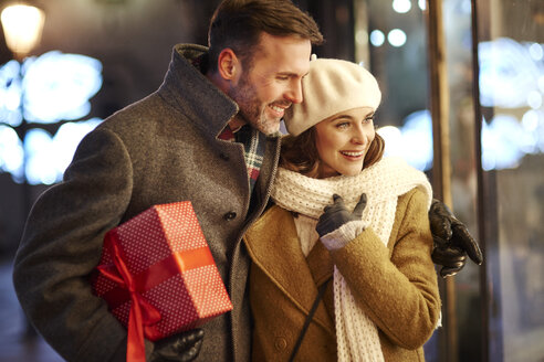 Glückliches Paar, das in ein Schaufenster zur Weihnachtszeit schaut - ABIF01154