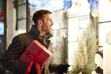 Smiling man with Christmas present looking in shop window - ABIF01157
