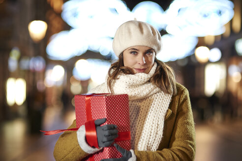 Porträt einer lächelnden Frau mit Weihnachtsgeschenk am Abend - ABIF01158