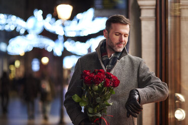 Porträt eines wartenden Mannes mit einem Strauß roter Rosen, der die Zeit kontrolliert - ABIF01162