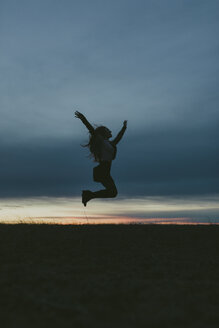 Silhouette einer glücklichen Frau in der Natur, die bei Sonnenuntergang in die Luft springt - JPF00350
