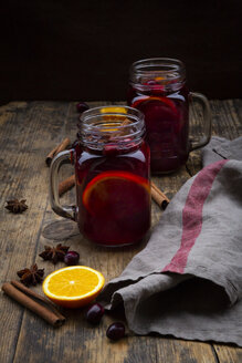 Gläser mit Glühwein, Preiselbeeren, Zimtstangen, Orange und Sternanis auf dunklem Holz - LVF07758