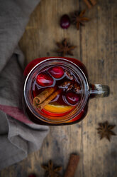 Glass of mulled wine with cranberries, cinnamon sticks, orange and star anise on dark wood, focus on foreground - LVF07759