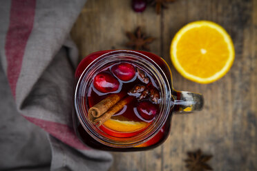 Glass of mulled wine with cranberries, cinnamon sticks, orange and star anise on dark wood, focus on foreground - LVF07760