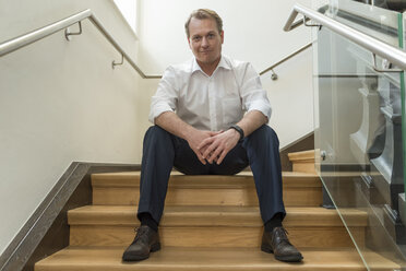 Portrait of confident businessman sitting in staircase - PAF01872