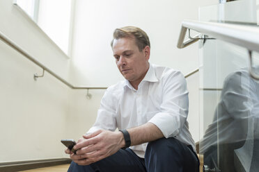 Businessman sitting in staircase using cell phone - PAF01874