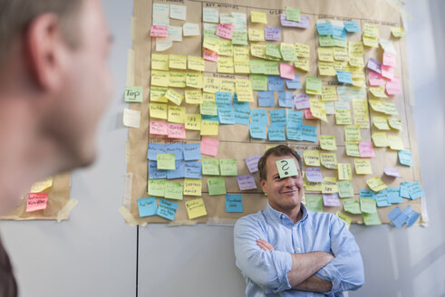 Businessman with sticky note sticking at his forehead in office - PAF01882