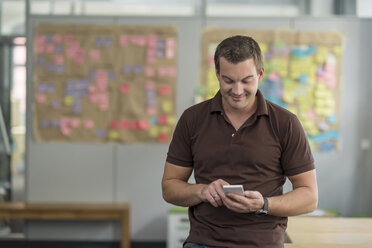 Smiling businessman using cell phone in office - PAF01894