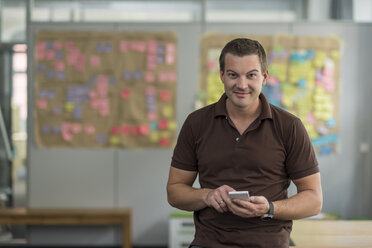 Portrait of smiling businessman with cell phone in office - PAF01895