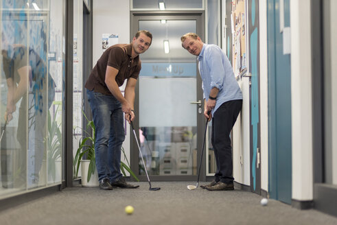 Two businessmen playing golf in office - PAF01903