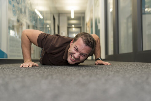 Businessman doing push-ups on office floor - PAF01910