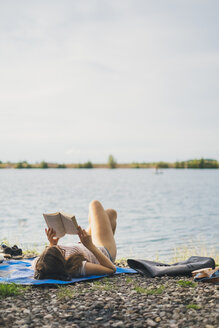 Junge Frau liegt auf einer Decke am Seeufer und liest ein Buch - JSCF00140