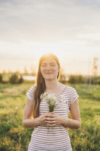 Porträt einer lächelnden jungen Frau mit einem Strauß gepflückter Wildblumen bei Sonnenuntergang - JSCF00144