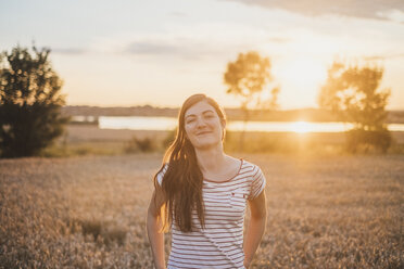 Porträt einer lächelnden jungen Frau in der Natur bei Sonnenuntergang - JSCF00148