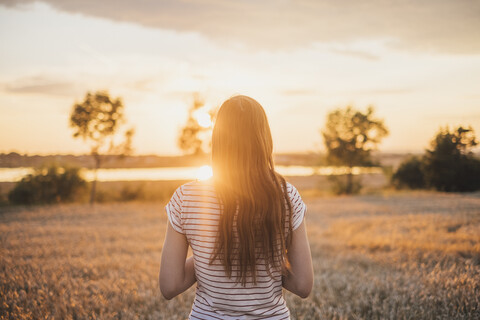 Rückenansicht einer jungen Frau bei Sonnenuntergang, lizenzfreies Stockfoto
