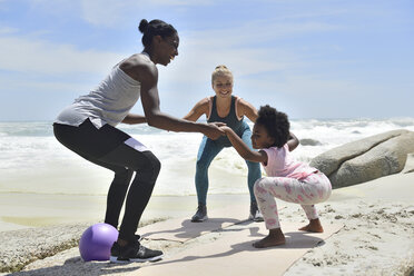 Mother with daughter and friend doing a fitness exercise on the beach - ECPF00384