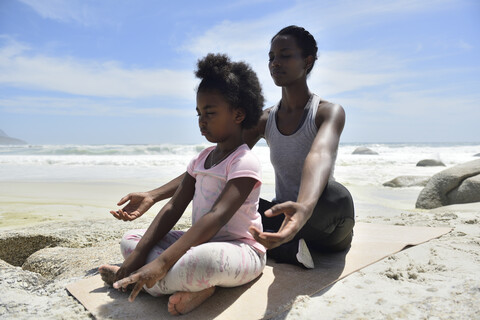 Mother with daughter doing a yoga exercise on the beach stock photo