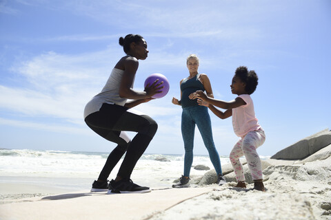 Mutter mit Tochter und Freund beim Training mit einem Ball am Strand, lizenzfreies Stockfoto