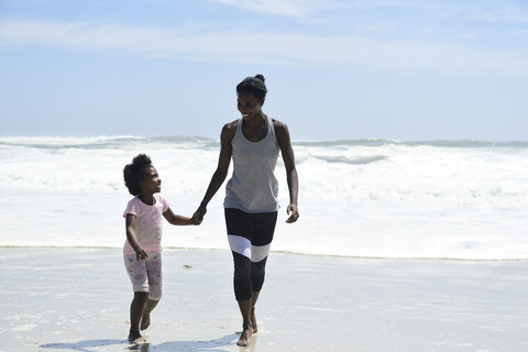 Mutter und Tochter gehen Hand in Hand am Strand spazieren, lizenzfreies Stockfoto