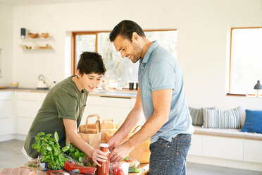 Boy and his father at kitchen counter unpacking groceries - CUF48510