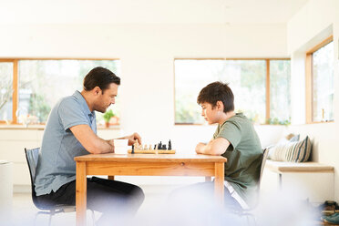 Boy and father playing chess at living room table - CUF48517