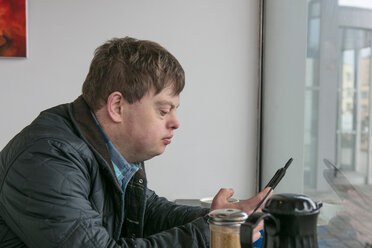 Mann mit Down-Syndrom telefoniert am Fenster eines Cafés - CUF48520