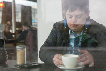 Mann mit Down-Syndrom trinkt Kaffee am Fenster eines Cafés - CUF48521