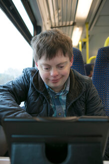 Man with down syndrome watching film on digital tablet on train - CUF48523
