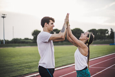 Male and female athlete high fiving on a tartan track - ACPF00459