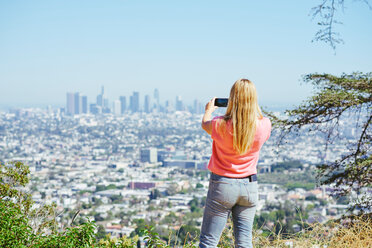 Junge Frau fotografiert die Skyline von einem Hügel aus, Rückansicht, Los Angeles, Kalifornien, USA - CUF48711