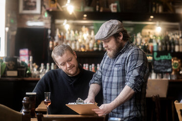 Barkeeper betrachtet mit einem Kunden die Speisekarte in einem traditionellen irischen Gasthaus - CUF48850