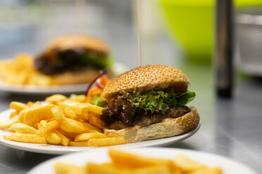 Teller mit Hamburgern und Pommes frites auf der Theke einer Großküche, Nahaufnahme - CUF48912