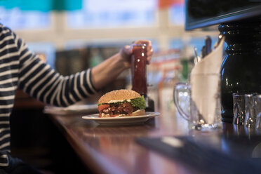 Frau mit Teller mit Burger auf dem Tresen einer Kneipe - CUF48936